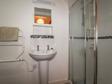 A bathroom with a pedestal sink mirror towel rack and a glass shower enclosure at Trenethick in Porthtowan
