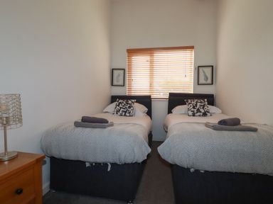 A bedroom with two single beds with patterned pillows and folded towels and a window with blinds at Trenethick in Porthtowan