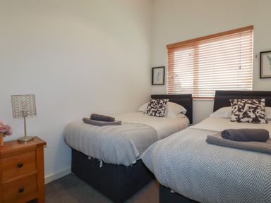 A bedroom with two single beds side by side with pillows and folded towels on them next to a wooden nightstand with a lamp and flowers at Trenethick in Porthtowan