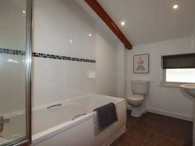 A bathroom with a bathtub a toilet a window and a framed picture at Trenethick in Porthtowan