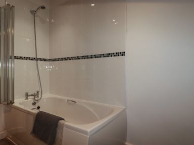 A bathroom with a bathtub shower and tiles on the wall at Trenethick in Porthtowan
