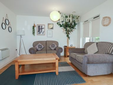 A living room with two striped sofas a wooden coffee table a floor lamp wall decorations and a large plant at Tregullan in Porthtowan