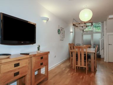 A dining room with a wooden table and chairs a wall mounted tv and glass doors at Tregullan in Porthtowan
