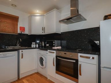 A kitchen with white cabinets a washing machine an oven a microwave and a refrigerator at Tregullan in Porthtowan