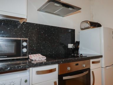 A kitchen countertop with a microwave oven a folded towel a knife block an electric stove oven a refrigerator and a bread box at Tregullan in Porthtowan
