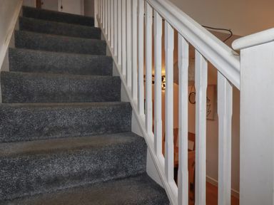 A carpeted staircase with white wooden railing and a dining area visible through the railing at Tregullan in Porthtowan