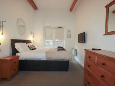 A bedroom with a bed nightstand wooden dresser wall-mounted tv and double doors at Tregullan in Porthtowan