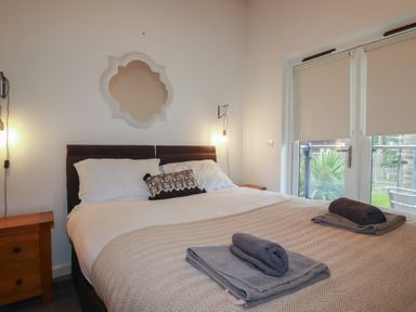 A bedroom with a double bed two bedside tables and a glass door with blinds at Tregullan in Porthtowan