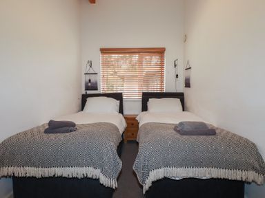 A bedroom with two single beds a window with wooden blinds and a bedside table at Tregullan in Porthtowan