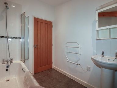 A bathroom with a bathtub shower combination a wooden door a wall-mounted heated towel rail and a pedestal sink with a mirror cabinet at Tregullan in Porthtowan