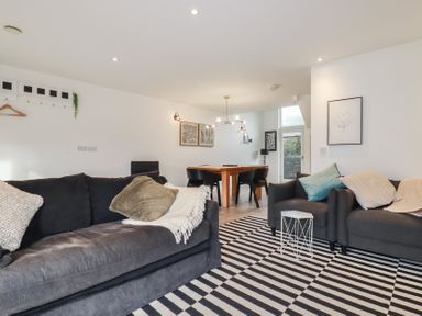 A living room with black sofas a striped rug and a wooden dining table with black chairs at Treveglos in Porthtowan