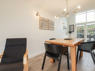 A dining room with a wooden table black chairs a black armchair wall art and large windows at Treveglos in Porthtowan