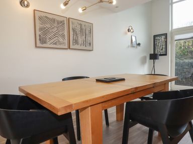 A dining room with a wooden table black chairs abstract wall art and a floor lamp at Treveglos in Porthtowan