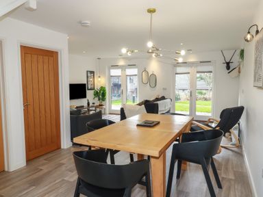A dining area with wooden table and black chairs connected to a living room with sofa and television at Treveglos in Porthtowan
