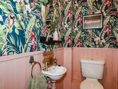A bathroom with a toilet and sink with tropical bird wallpaper and pink paneling at Treveglos in Porthtowan