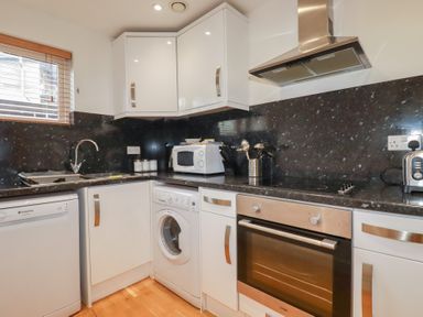 A kitchen with white cabinets black countertops a washing machine microwave oven and cooking utensils at Treveglos in Porthtowan