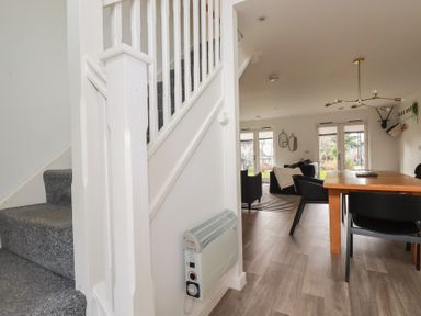 A dining area with a wooden table and black chairs next to a living room with sofas and windows at Treveglos in Porthtowan
