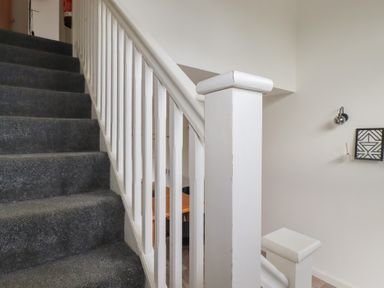 A staircase with grey carpet and white banister with a wall lamp and framed art on the wall at Treveglos in Porthtowan