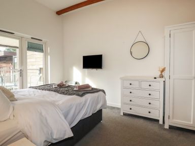 A bedroom with a bed and white linens a dresser with a mirror on the wall and a TV mounted on the wall at Treveglos in Porthtowan