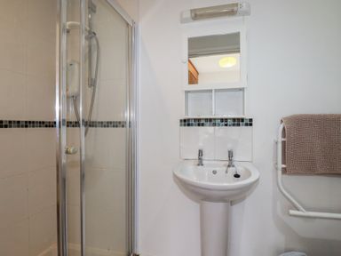 A bathroom with a shower enclosure a sink with two taps a mirror and a towel on a rack at Treveglos in Porthtowan