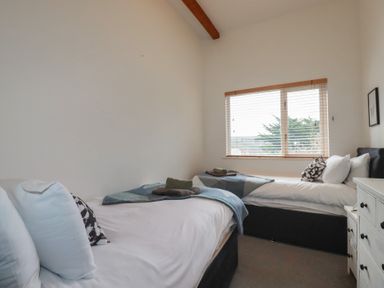 A bedroom with two single beds near a window with blinds and a white chest of drawers at Treveglos in Porthtowan