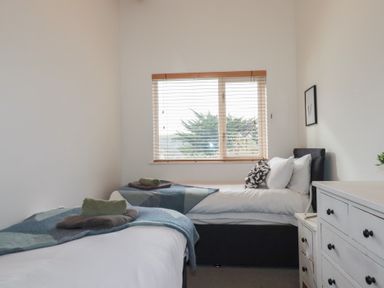 A bedroom with two beds a window with blinds and a white chest of drawers at Treveglos in Porthtowan