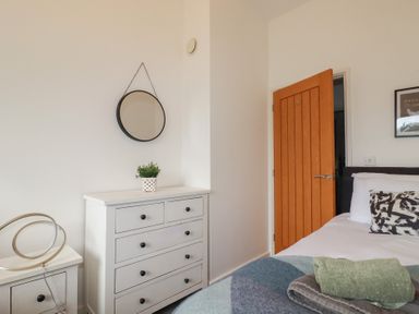 A bedroom with a white chest of drawers a round mirror on the wall a wooden door and a bed with pillows and folded towels at Treveglos in Porthtowan