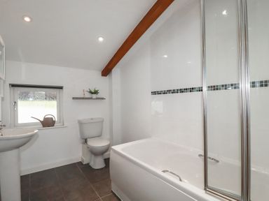 A bathroom with a bathtub shower screen toilet pedestal sink window and a wooden beam on the ceiling at Treveglos in Porthtowan
