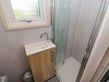 A small bathroom with a wooden vanity cabinet and a white sink next to a glass shower enclosure at Little Acre in Oxenhope