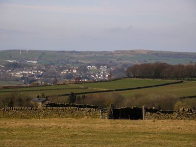 A rural landscape with stone walls and green fields with a village and hills in the background at Little Acre in Oxenhope