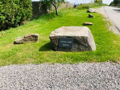 A sign for Little Acre with rocks and grass at Little Acre in Oxenhope