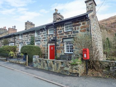 A stone cottage with a red front door and a red post box outside at Llety in Beddgelert