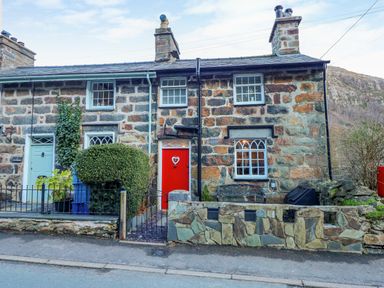 A stone house with a red door and a bench outside at Llety in Beddgelert