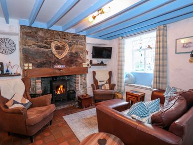 A living room with a stone fireplace and wood stove two armchairs a leather sofa and a window seat at Llety in Beddgelert