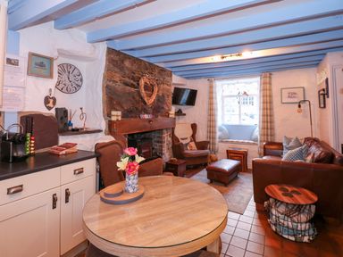 A living room with a round wooden table, armchairs, a stone fireplace, a leather sofa, and a window seat at Llety in Beddgelert