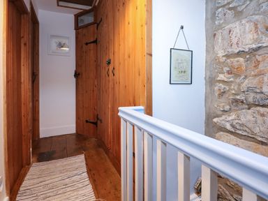 A hallway with wooden doors a white railing and a stone wall at Llety in Beddgelert