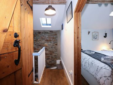 A hallway with wooden floor and door leading to a bedroom with a bed and wall decorations at Llety in Beddgelert