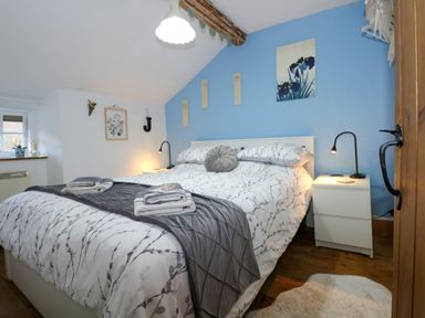 A bedroom with a double bed white nightstands and floral wall art at Llety in Beddgelert