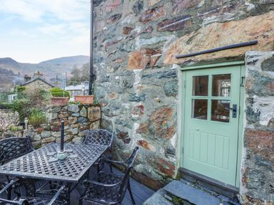 A stone patio with a black metal table and chairs next to a light green door at Llety in Beddgelert