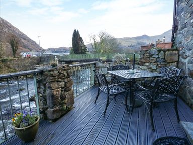 An outdoor patio with metal table and chairs next to a river and stone walls at Llety in Beddgelert