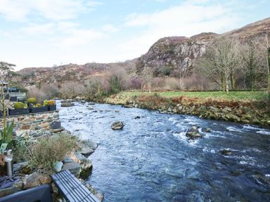 A river flowing between rocky banks with hills and trees in the background at Llety in Beddgelert