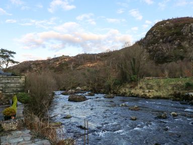 A flowing river with rocks surrounded by trees and hills at Llety in Beddgelert