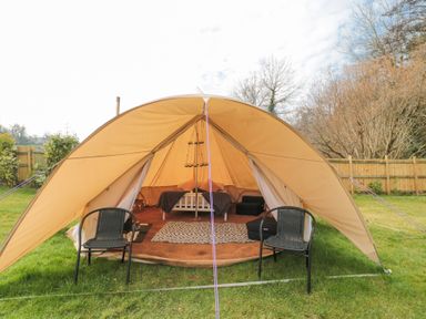 A bell tent with two chairs outside a bed and rug inside surrounded by grass and trees at Bell tent 2 Camerton near Timsbury