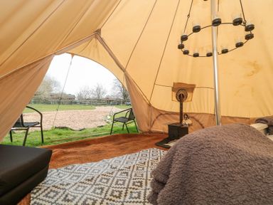 The interior of a bell tent with a wood stove a kettle a circular candle holder two chairs and outdoor view at Bell tent 2 in Camerton near Timsbury