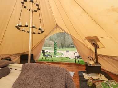 Inside a bell tent with a bed covered by a blanket a wood stove with a kettle and two chairs outside on grass at Bell tent 2 in Camerton near Timsbury