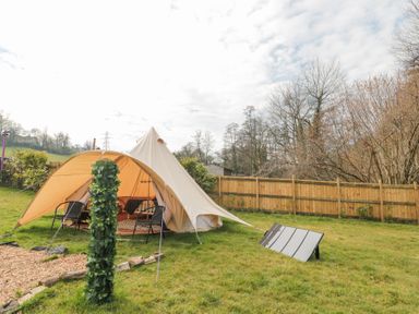 A beige bell tent set up on grassy ground with chairs inside and a wooden fence in the background at Bell tent 2 Camerton near Timsbury