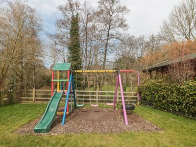 A playground with a slide and swings in a garden surrounded by trees and fencing at Bell tent 2 in Camerton near Timsbury