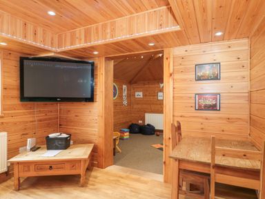 A wooden room with a wall-mounted TV table and chairs near a small adjoining playroom at Bell tent 2 in Camerton near Timsbury