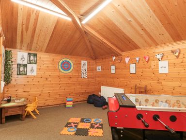 A wooden playroom with a foosball table a small table and chair tic tac toe game and a dart board at Bell tent 2 in Camerton near Timsbury
