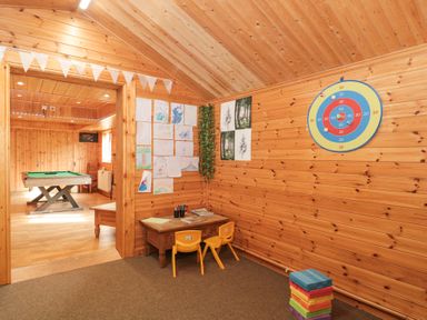 A wooden room with a small table and two yellow chairs with drawings on the wall and a dartboard at Bell tent 2 in Camerton near Timsbury